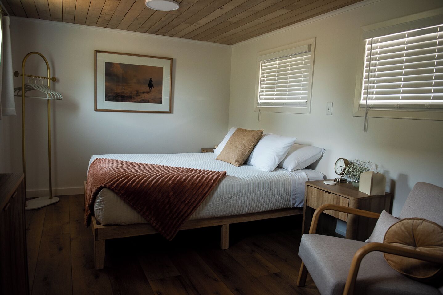A bedroom with a bed, bedside table, chair, and a painting on the wall.