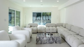 A modern living room with a sectional sofa, a marble coffee table, and a large sliding glass door leading to a pool area.