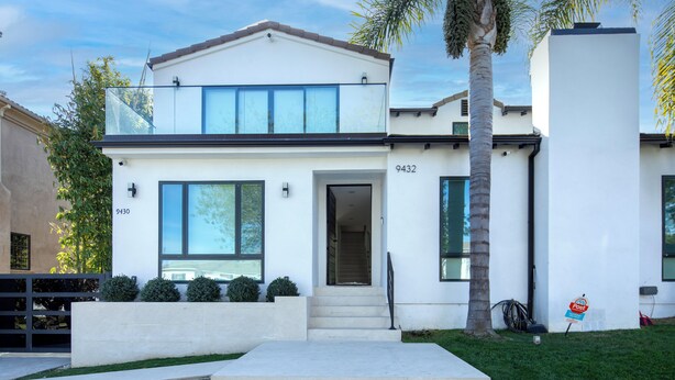A modern two-story house with a flat roof, large windows, and a visible address number.