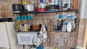 A compact kitchen with a microwave, stove, sink, and various kitchen utensils and cookware. - Apartamento Salvador Praia (Salvador)