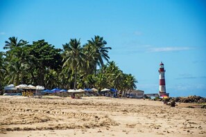 Una playa con un faro, palmeras y sombrillas.