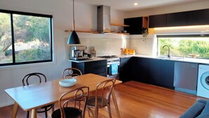 A modern kitchen with a dining area, featuring a wooden table, chairs, a coffee machine, and a built-in oven.