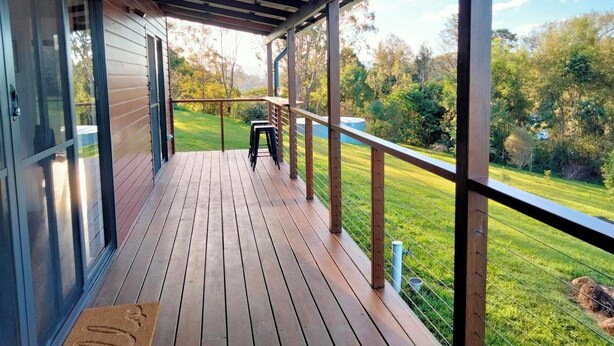 A covered deck with a wooden floor, a metal railing, and a view of a grassy area with trees.
