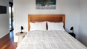 A bedroom with a wooden headboard, white bedding, and a painting of flowers on the wall.