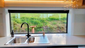 A kitchen with a stainless steel sink, a window with a view of a grassy area, and a wine rack above the sink.