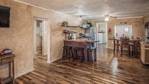 A spacious kitchen with wooden flooring, a central island with stools, and a dining area with wooden chairs. - Cuddle Up In the Upper Canyon! (Ruidoso)