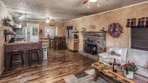 A spacious living room with a fireplace, wooden flooring, and a dining area. - Cuddle Up In the Upper Canyon! (Ruidoso)