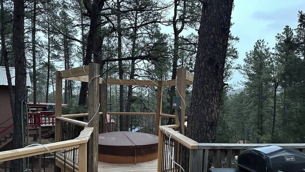 A wooden deck with a hot tub, a barbecue grill, and a wooden pergola structure. - Cuddle Up In the Upper Canyon! (Ruidoso)