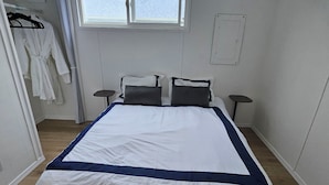 A neatly made bed with a white and blue bedspread, two bedside tables, and a window with blinds. - Enjoyable 3-bedroom house with access to the beach (Long Beach)