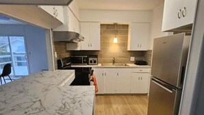 A modern kitchen with white cabinets, a marble countertop, and a stainless steel refrigerator. - Enjoyable 3-bedroom house with access to the beach (Long Beach)