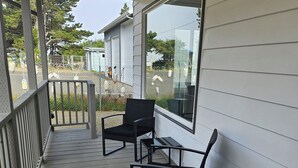 A covered porch with two black chairs and a small table. - Enjoyable 3-bedroom house with access to the beach (Long Beach)