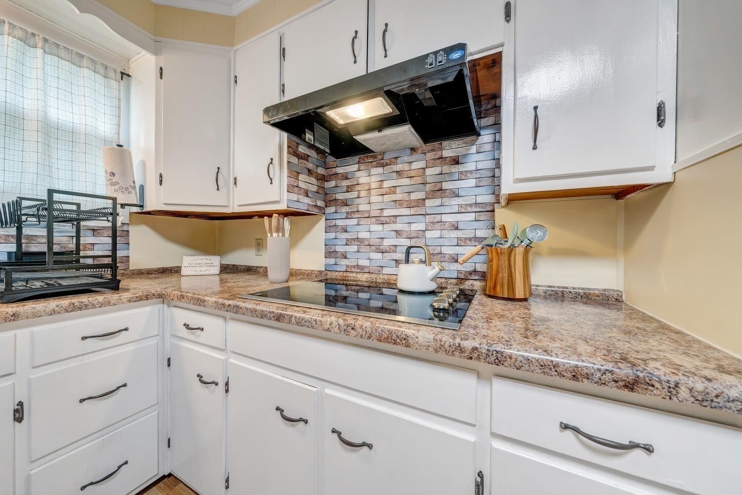 A kitchen with white cabinets, a granite countertop, a brick backsplash, and a stainless steel range hood.