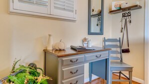 Una habitación con escritorio, silla y espejo. Se observa una estantería con llaves y una planta pequeña.