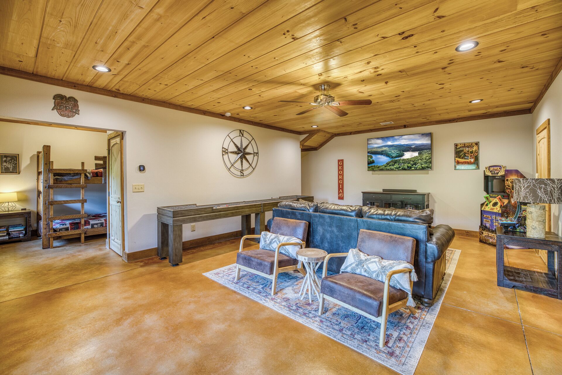 A cozy living room with a wooden ceiling, a pool table, a blue sofa, and a gaming area.