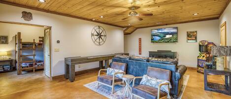 A cozy living room with a wooden ceiling, a pool table, a blue sofa, and a gaming area.