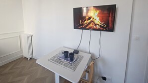 A room with a white wall, a mounted television displaying a fireplace, a small table with a tray, and a radiator. - Studio Cozy Ivry near Paris (Ivry-sur-Seine)