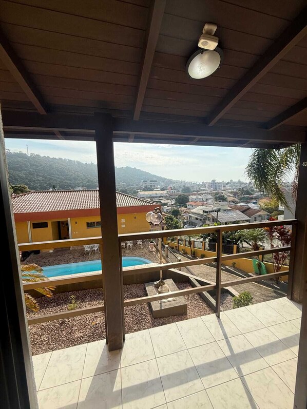 Un espacio exterior cubierto con vistas a un barrio residencial, una piscina y un suelo de baldosas.