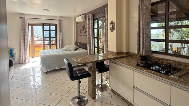 Una cocina moderna con una isla central, una zona de comedor con sofá y un dormitorio con balcón.