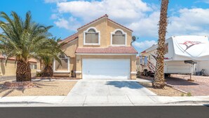 A two-story house with a red-tiled roof, a white garage door, and a satellite dish. - Patio w/ Grill + Pool Table , In-Unit Laundry (North Las Vegas)
