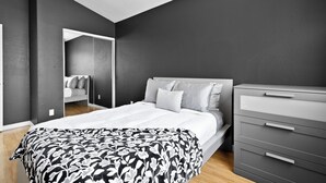A modern bedroom with a large bed, a dresser, and a mirror. - Patio w/ Grill + Pool Table , In-Unit Laundry (North Las Vegas)