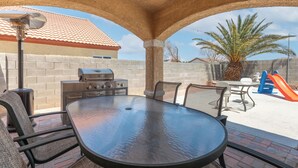 An outdoor patio area with a round table and chairs, a grill, and a slide. - Patio w/ Grill + Pool Table , In-Unit Laundry (North Las Vegas)