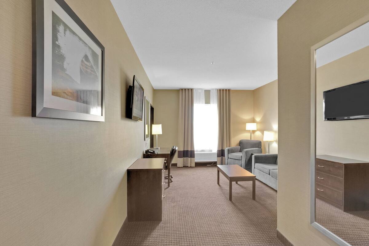 A hotel room with a bed, a desk, a chair, a TV, and a window with curtains.
