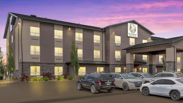 Ein Hotel mit modernem Design, das eine Steinfassade und viele Fenster aufweist. Vor dem Hotel befinden sich mehrere parkende Autos, und ein Schild kennzeichnet es als Duvernay Inn & Suites.