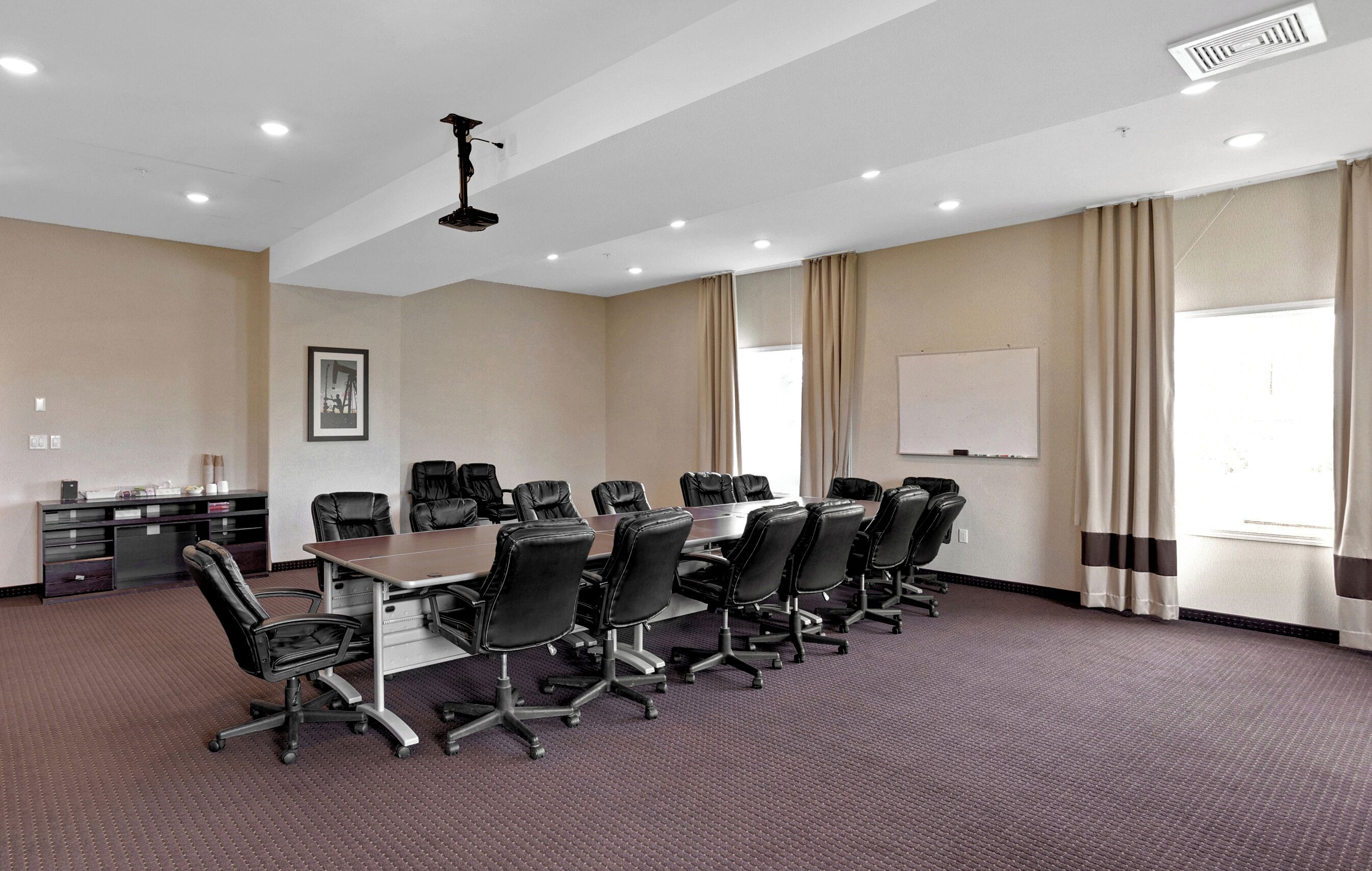 Un salón de conferencias con una larga mesa, varias sillas, una pizarra y una ventana con cortinas.