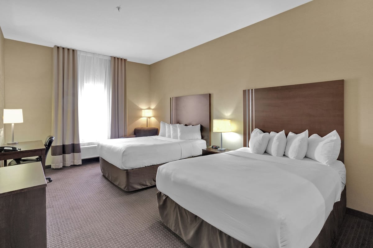 A hotel room with two beds, a desk, and a chair.