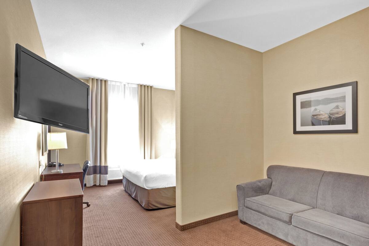 A hotel room with a bed, a TV, a desk with a lamp, a couch, and a framed picture on the wall.