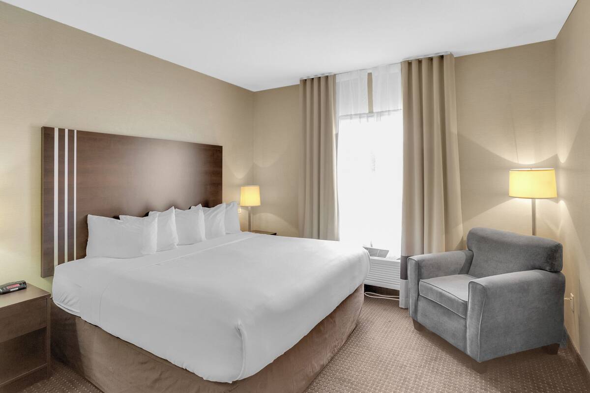 A hotel room with a large bed, a chair, a nightstand, a lamp, and a window with curtains.