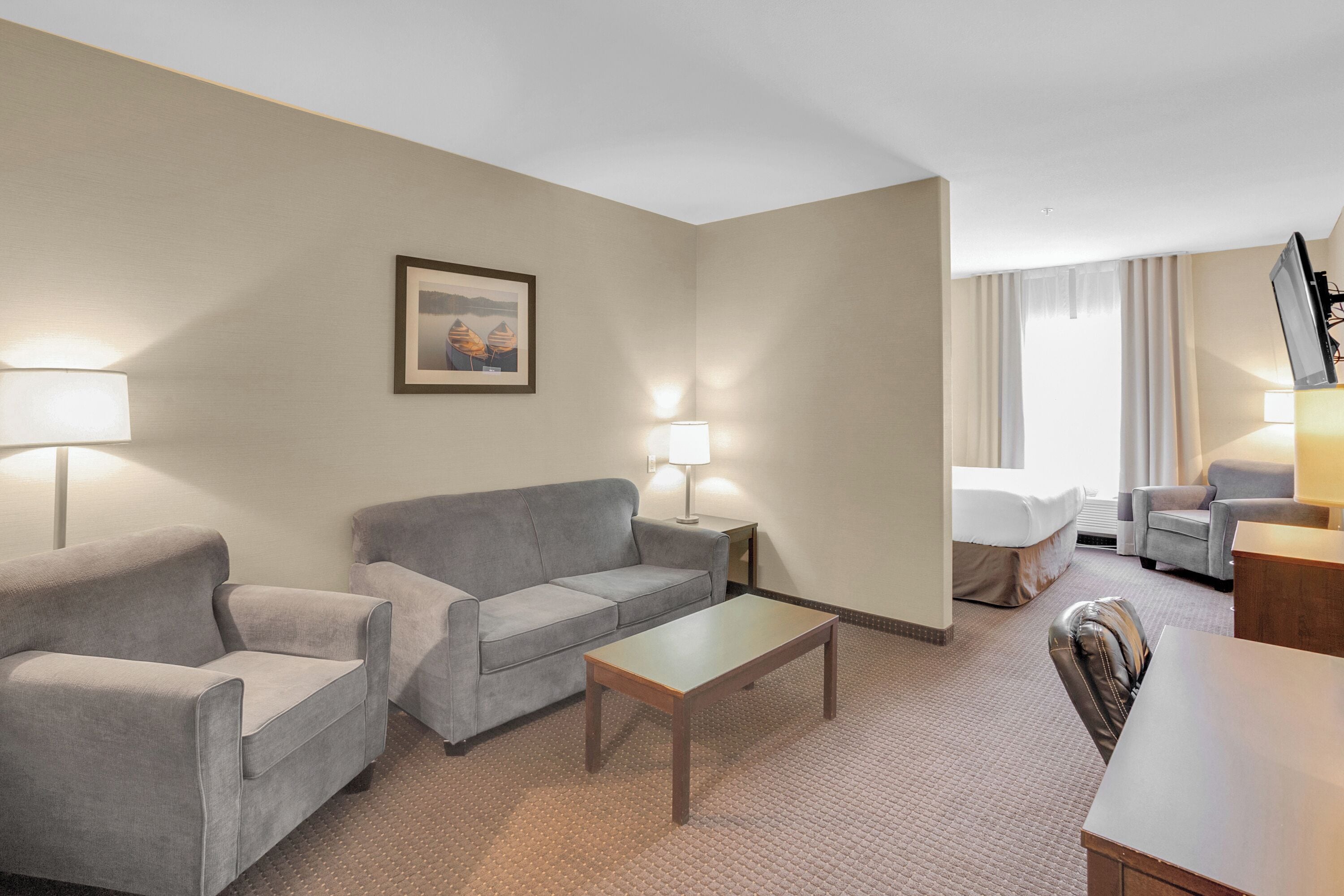 Ein Hotelzimmer mit grauem Sofa, einem Holztisch und einem Fernseher auf einem Schrank.
