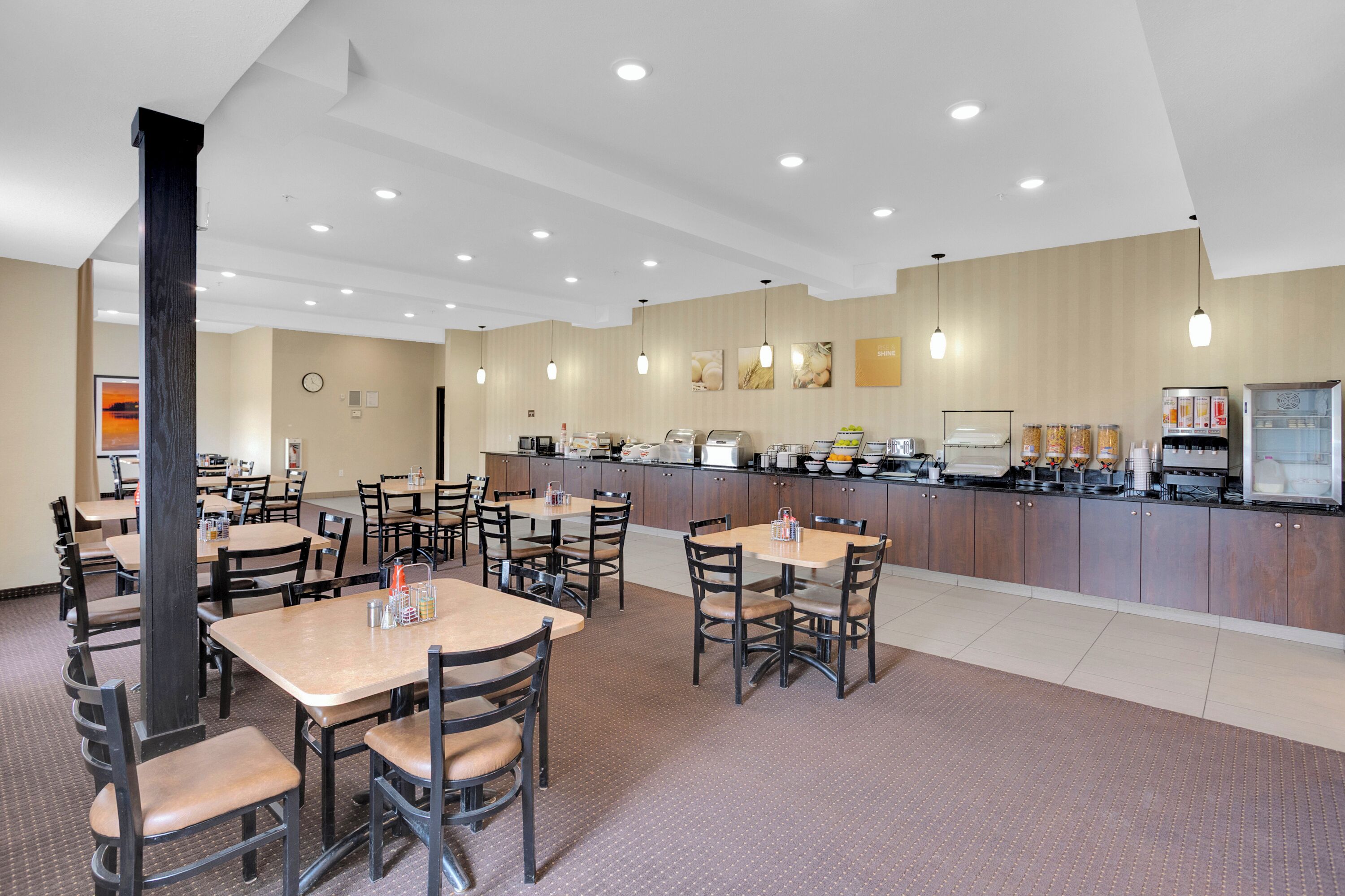 A spacious dining area with multiple tables and chairs, a self-service beverage station, and a clock on the wall.