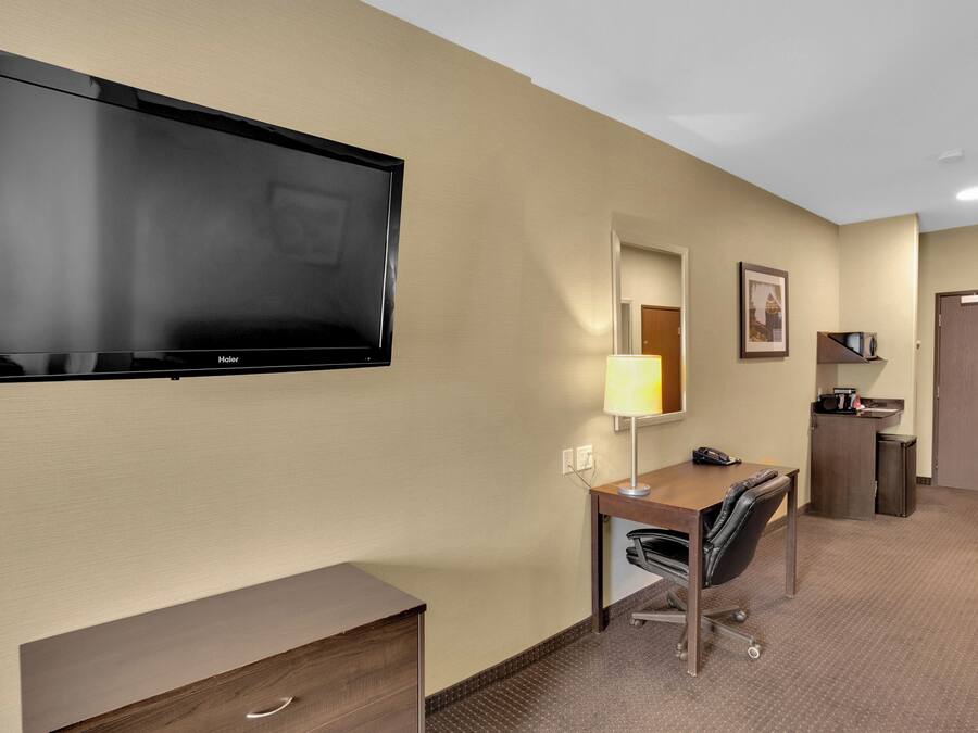 A hotel room with a flat-screen TV, a desk with a chair, a lamp, a mirror, a small cabinet, and a door.