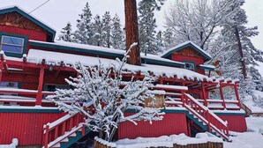 Une cabane rouge, dont le toit est recouvert de neige, et un escalier en bois qui mène à l’entrée.