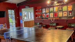 Une table de ping-pong dans une pièce avec un mur rouge, un panneau indiquant l’emplacement de la cuisine et un tableau d’affichage orné d’affiches annonçant diverses activités.