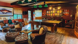Une pièce chaleureuse avec une table de billard, des fauteuils en cuir, une bibliothèque et un panneau indiquant les activités proposées.