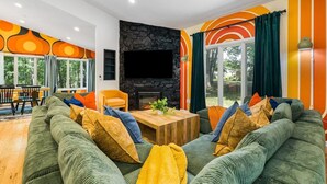 A modern living room with a stone fireplace, green sofas, and a dining area with a table and chairs.