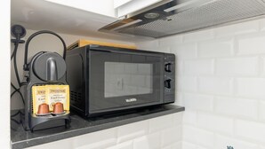 Een keuken met een zwarte magnetron, een koffieapparaat en een witte betegelde spatwand.