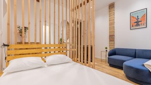 Een moderne slaapkamer met een houten hoofdeinde, een blauwe bank en een bed met witte lakens.