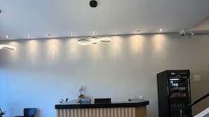 Un espace d’accueil comprenant un comptoir de réception en bois, un fauteuil noir, une plante et un distributeur automatique.