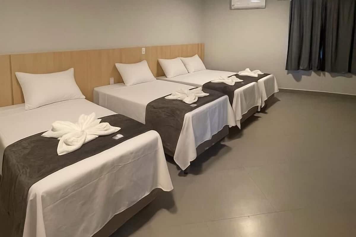 A hotel room with three beds, each with white bedding and a towel on the bed.