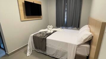 Ein modernes Hotelzimmer mit Bett, Wandfernseher und einem Fenster mit Vorhängen.