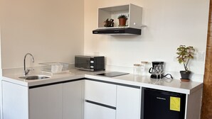 A modern kitchen with white cabinetry, a black dishwasher, a microwave, and a small shelf with decorative items. - Fantastic Restored Patrimonial Suite (Cuenca)