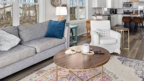A modern living room with a grey sofa, a coffee table, and a patterned rug. - Charming 3-bedroom cottage in Coral with WiFi and AC (Coral)