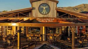A waterfront restaurant with outdoor seating, a prominent circular window with a figure, and a sign stating "Wine is sunlight held together by Water." - The Grape Escape/Luxury Stay/Views/Walk 2 Old Town (Cottonwood)
