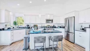 A modern kitchen with white cabinetry, stainless steel appliances, and a central island with bar stools. - The Grape Escape/Luxury Stay/Views/Walk 2 Old Town (Cottonwood)