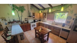 Une cuisine avec des meubles en bois, une table à manger et une fenêtre avec des stores.