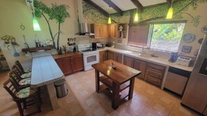 Una cocina con armarios de madera, una mesa de comedor y un ventanal con persianas.