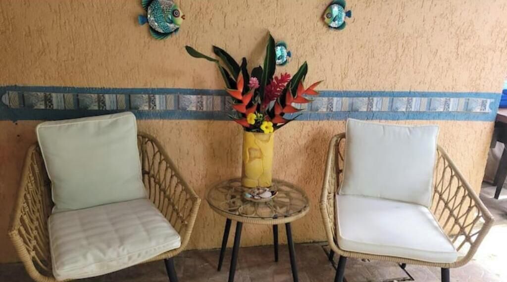 Two wicker chairs with cushions, a small round table, and a vase with flowers on a textured wall.